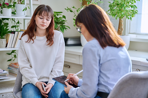Teenage girl college student at therapy meeting with mental health professional social worker psychologist counselor sitting together in office. Psychologists, psychotherapy, mental assistance support