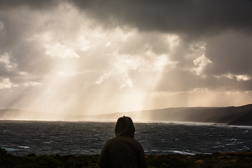 Rough windy ocean with dramatic light coming from storm clouds and a silhouetted person watching. Photographed off the south west coast of Western Australia.