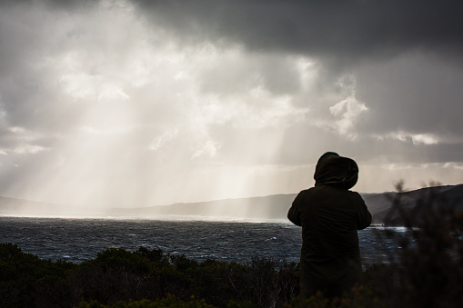 Rough windy ocean with dramatic light coming from storm clouds and a silhouetted person watching. Photographed off the south west coast of Western Australia.