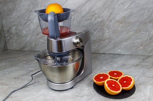 Modern electric juicer and grapefruits on a kitchen table. Preparing fresh squeezed grapefruit juice