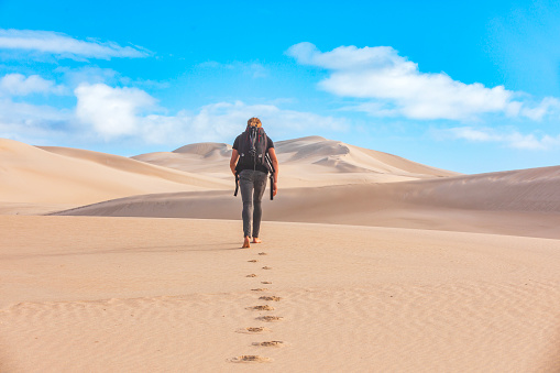One lonely man walks in desert on dunes