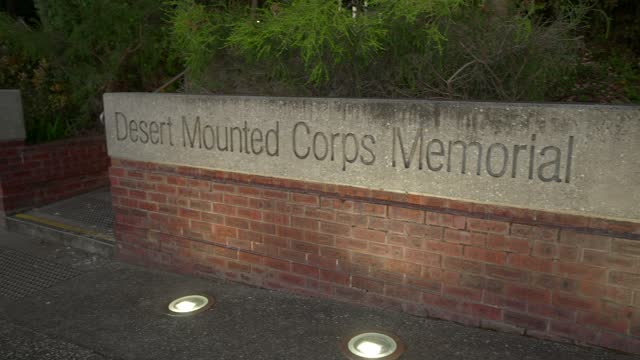 Panning and tilt up reveal of the lit up entrance sign to the Desert Mounted Corps Memorial at dawn.
