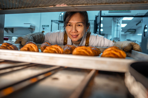 female baker taking off baked items from over in bakery kitchen