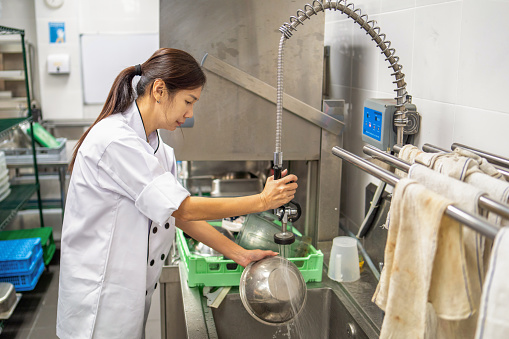female chef spraying water and washing utensils working in commercial kitchen