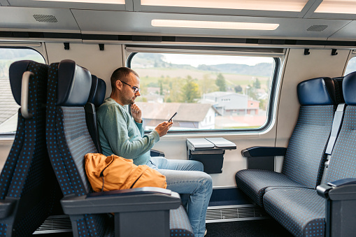 Handsome mid-adult man using a smart phone while riding in a train in Switzerland.