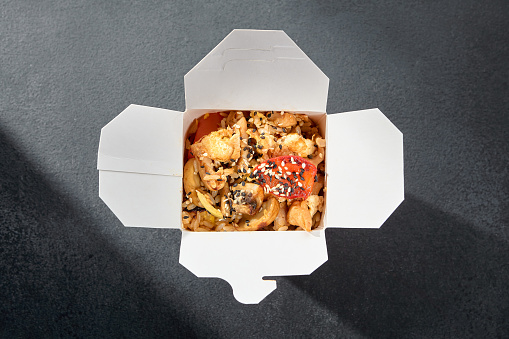 Stir-fried rice with chicken and vegetables in a wok, served in a takeaway box, ideal for a fast and fulfilling Asian-inspired meal.