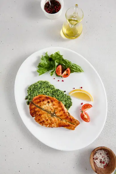 Pan-seared salmon steak with fresh spinach on white plate, perfect for healthy lifestyle and seafood cuisine presentations.