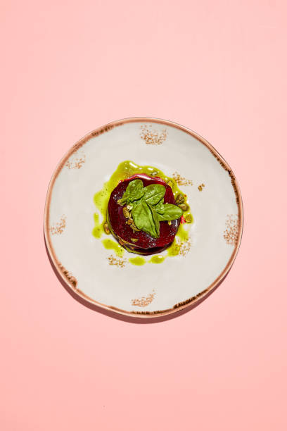 Top view of beetroot mille-feuille with pesto sauce on an elegant plate, presented on a soft pink background
