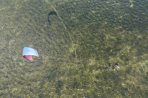 People swim in the sea on a kiteboard or kitesurfing. Summer sport learning how to kitesurf. Kite surfing on Puck bay in Jastarnia, Poland, Europe aerial drone photo