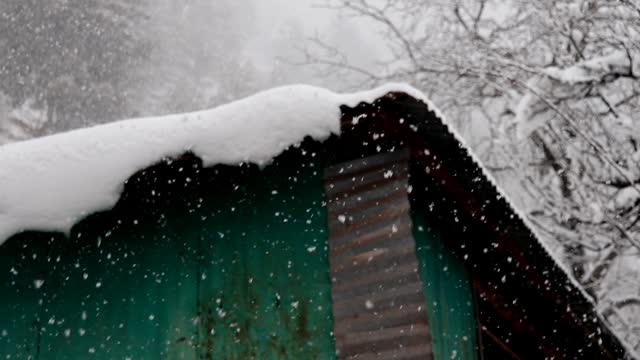 Snowfall on the cabin roof in the forest. Heavy snowfall.