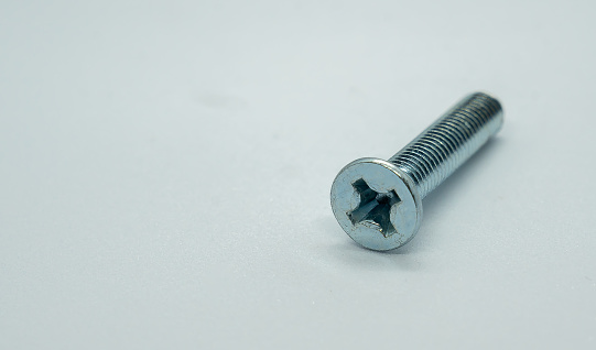 A close-up of a lone screw resting on a white background
