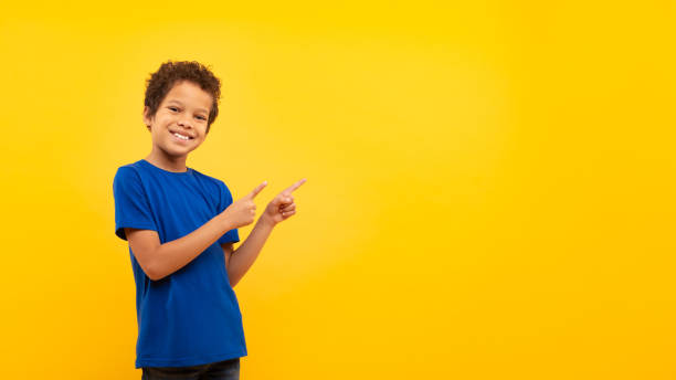 istock Latin boy with bright smile pointing at copy space against yellow backdrop 1994798568
