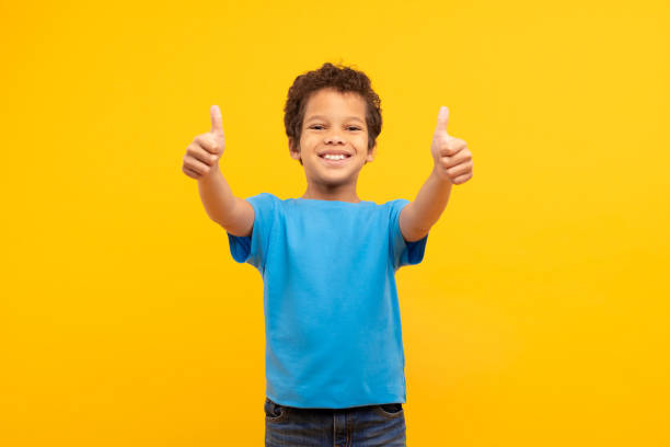 istock Cheerful boy with thumbs up in blue, vibrant yellow background 1994798583
