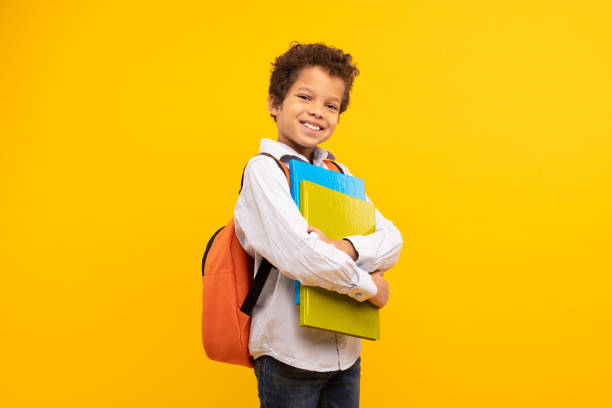 istock Schoolboy with books and backpack, confident on yellow backdrop 1994799091