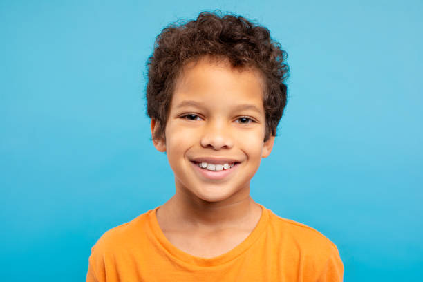 istock Cheerful curly-haired boy in orange t-shirt, blue background 1994799106