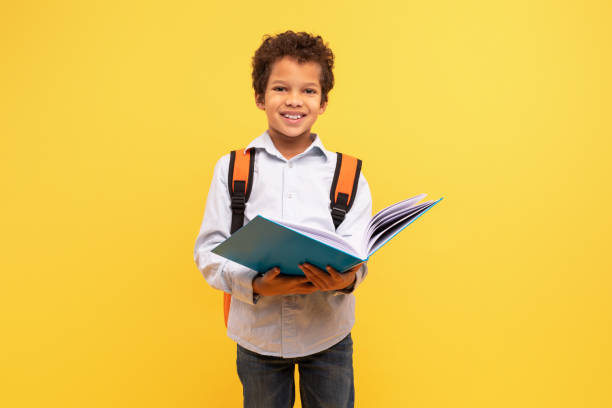 istock Schoolboy reading book with backpack on yellow background 1994799116
