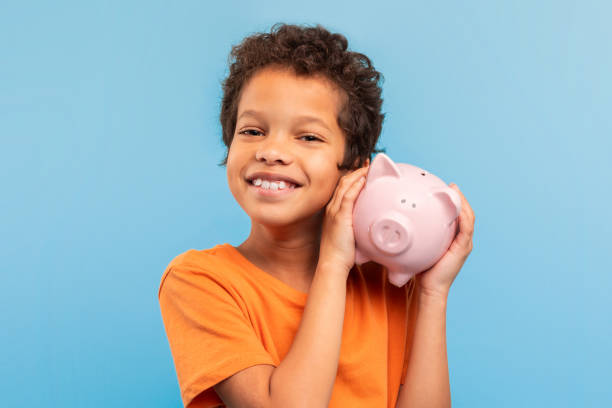 istock Smiling boy holding piggy bank on blue background 1994799131