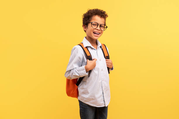 istock Happy black schoolboy with backpack smiling on yellow backdrop 1994799132