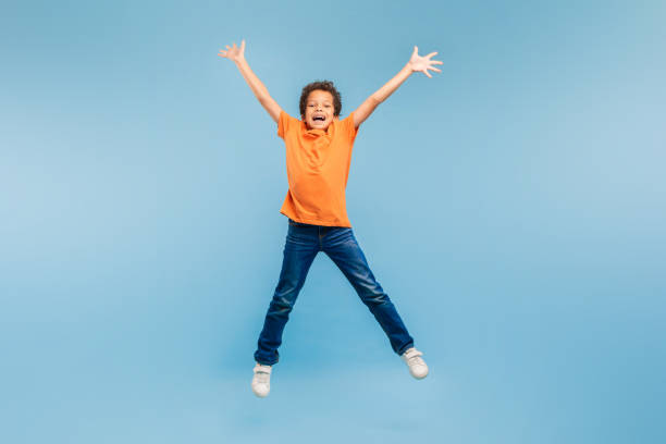 Joyful boy jumping with arms wide open on blue background