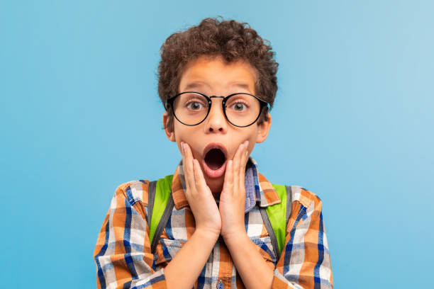 istock Shocked boy with glasses, hands on cheeks, blue background 1994799156