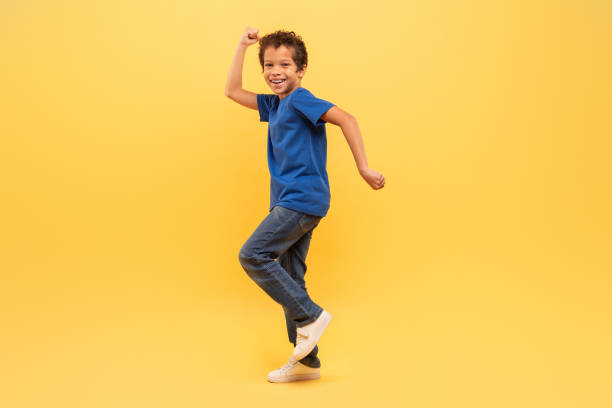 istock Joyful boy dancing in blue shirt on yellow background 1994799163