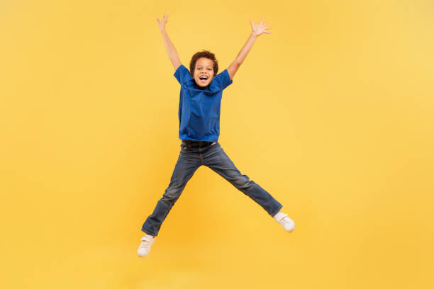 Ecstatic boy jumping high with arms up on yellow background