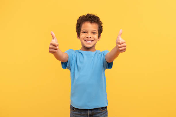 istock Joyful boy with double thumbs up in blue on yellow background 1994799674