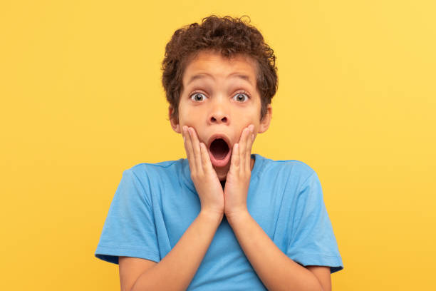 istock Shocked boy with hands on face, open mouth on yellow background 1994799683