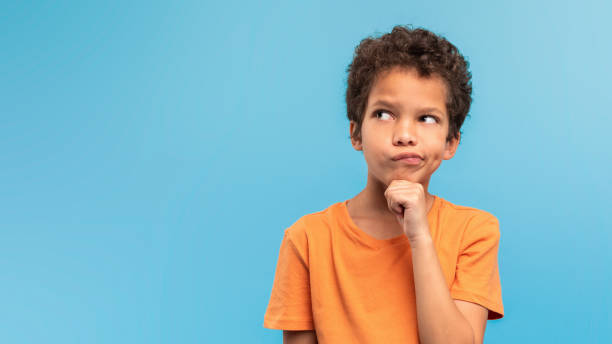 istock Thoughtful boy in orange, pondering on blue background, free space 1994799701