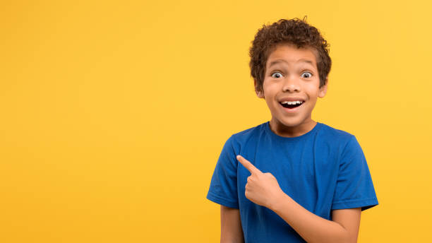 istock Excited boy pointing, blue shirt, yellow wall 1994799717