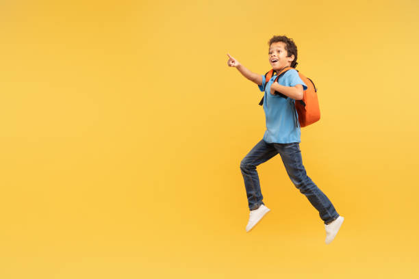 istock Boy in mid-stride pointing excitedly, yellow backpack 1994799722