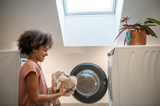 Young girl doing laundry, washing machine open.
