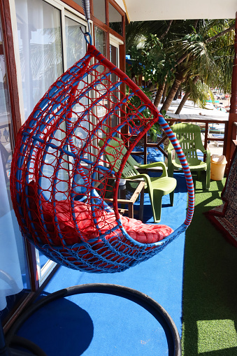 Stock photo showing close-up view of hanging, ball chair on beach hut balcony overlooking Palolem Beach, Goa, India.