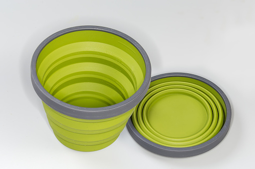 Two empty tourist foldable cups made of food-grade flexible thermo silicone in the folded and unfolded state on a gray surface