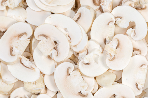 Background of the fresh uncooked button mushrooms chopped into thin slices, top view