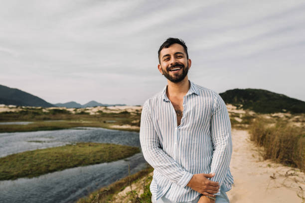 Portrait of a young man smiling while standing on a sandy footpath during a walk along a scenic coastline