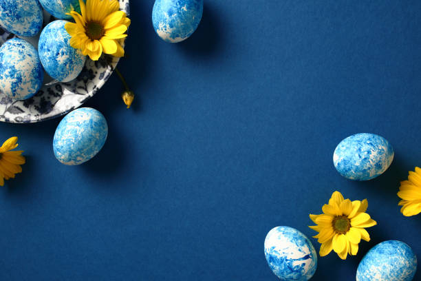 istock Blue and white handmade Easter eggs with yellow flowers on dark blue background. Flat lay, top view. 1994850270
