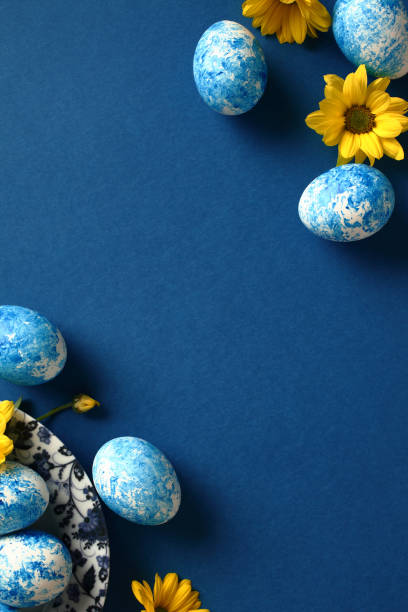 istock Blue and white handmade Easter eggs with yellow flowers on dark blue background. Flat lay, top view. 1994850818