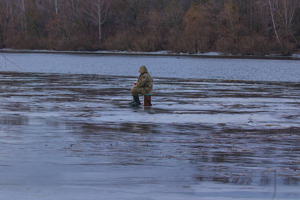 Mature man relaxing while fishing in mountain lake in waders during overcast weather, enjoying solitude & connecting with nature. Getting away from it all