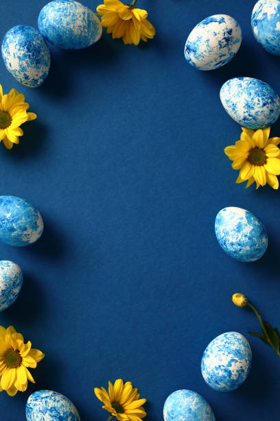 istock Easter vertical background, poster, banner design. Frame of blue and white painted Easter eggs with yellow flowers on dark blue background. 1994853503