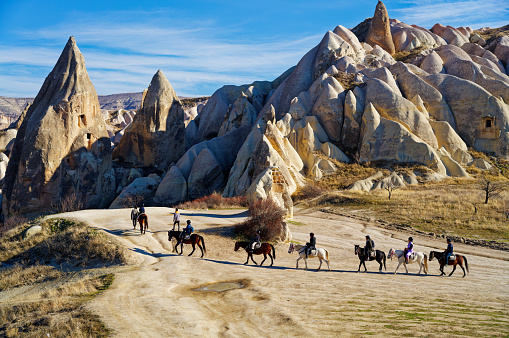 People riding horses on the Rose Red Valley in Cappadocia, Turkey. Famous destination for people to explore the Rock Sites of Cappadocia.