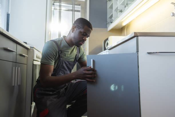 Photo of young carpenter repairing the kitchen unit under the sink in the kitchen