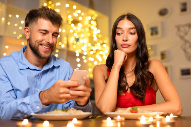 istock Man on phone smiling, woman bored at candlelit dinner 1994892944