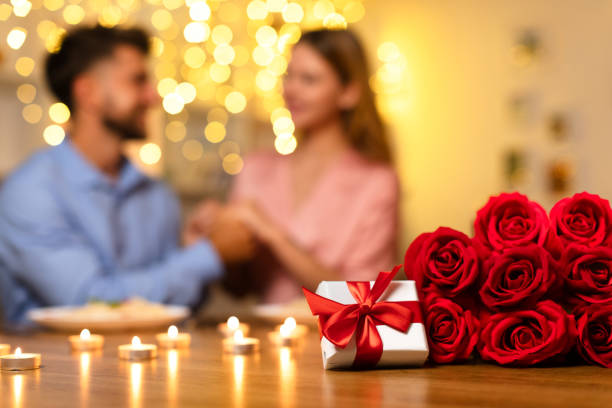 istock Man surprises partner with gift and roses during romantic candlelit dinner 1994892994