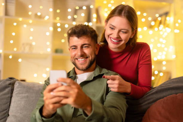 istock Cheerful couple looking at smartphone with festive lights backdrop 1994893561