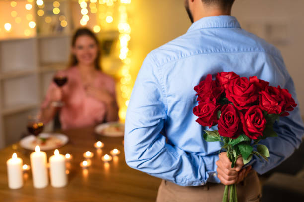 istock Surprised woman with wine as man approaches with roses 1994893583