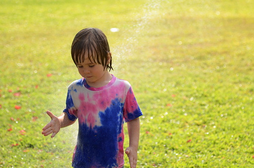 Little boy playing with garden sprinkler. Preschooler Boy running and jumping. Summer outdoor water fun in the backyard. Children play with hose watering grass. Kids run and splash on hot sunny day.