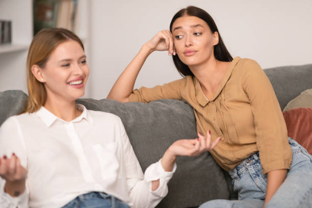 Jealous Lady Listening To Her Cheerful Friend Talking At Home Envy In Friendship. Jealous Lady Listening To Her Cheerful Friend Talking And Bragging About Her Great Life Sitting On Couch At Home, Rolling Eyes During Conversation. Selective Focus rolling eyes irritation displeased facial expression stock pictures, royalty-free photos & images