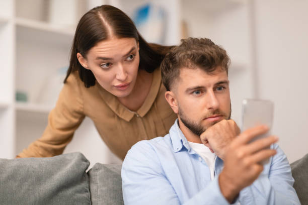 istock Jealous Girlfriend Spying On Boyfriend While Chatting On Smartphone Indoors 1994911870