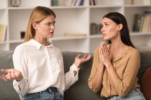 Mature mother feeling displeased while arguing with her adult daughter at home.